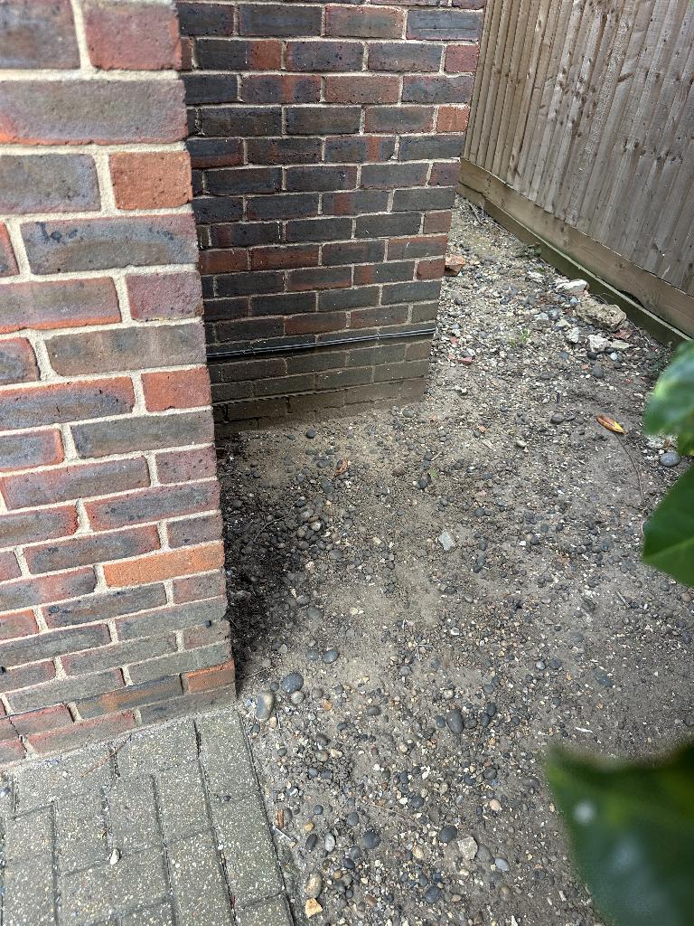 After clearance in Bromley Town: the enclosed yard area beside the brick wall and fencing is cleared, leaving an open surface with smaller remaining gravel-like debris distributed across the ground rather than piled waste.